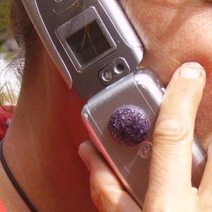 Hand holding flip phone with small dark purple orgonite piece placed on top of device