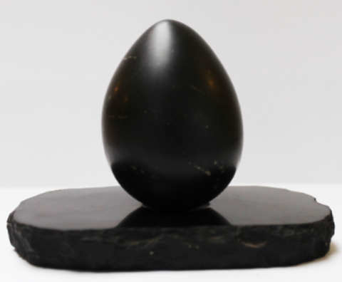 Black polished egg-shaped stone sitting on black oval base against white background