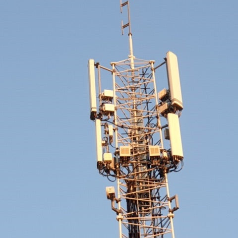 Cell phone tower with multiple antennas and equipment mounted on metal framework against clear blue sky