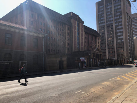 Urban street scene with historic stone building and modern high-rise tower, person walking on sidewalk, bright sunlight