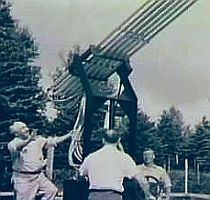Black and white photo showing people gathered around a large multi-barreled artillery weapon or rocket launcher in an outdoor setting