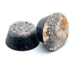 Two round disc-shaped objects: left is black with speckled texture, right has silver metallic surface with decorative pattern