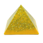 Yellow translucent orgonite pyramid with metallic shavings embedded throughout, photographed against white background