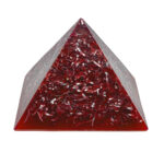 Clear triangular orgonite pyramid with red metallic shavings suspended inside, photographed against white background