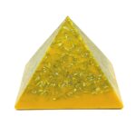 Yellow triangular orgonite pyramid with metallic shavings embedded throughout, viewed from front angle on white background
