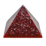 Red translucent orgonite pyramid with metallic spirals and shavings embedded inside, viewed from front angle