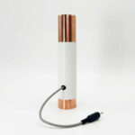 Tube cylindrique blanc avec capuchons métalliques couleur cuivre aux extrémités, relié à un câble gris avec prise jack noire
