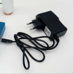 Adaptateur secteur noir avec fiche EU et câble noir attaché avec connecteur, posé sur surface blanche