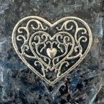 Ornement doré métallique en forme de cœur avec motif de filigrane tourbillonnant, petit cœur au centre, sur surface sombre