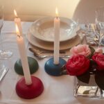 Three round orgonite candle holders in red, green, and blue with lit white candles on elegant table setting with flowers and glassware