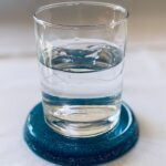 Clear glass with water sits on dark blue circular dolomite coaster on white surface
