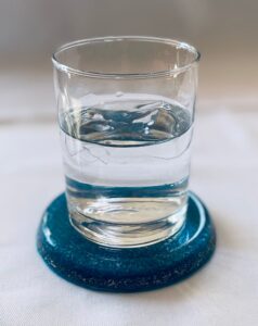 Clear glass with water sits on dark blue circular dolomite coaster on white surface