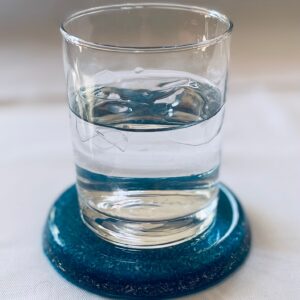 Clear glass with water sits on dark blue circular dolomite coaster on white surface