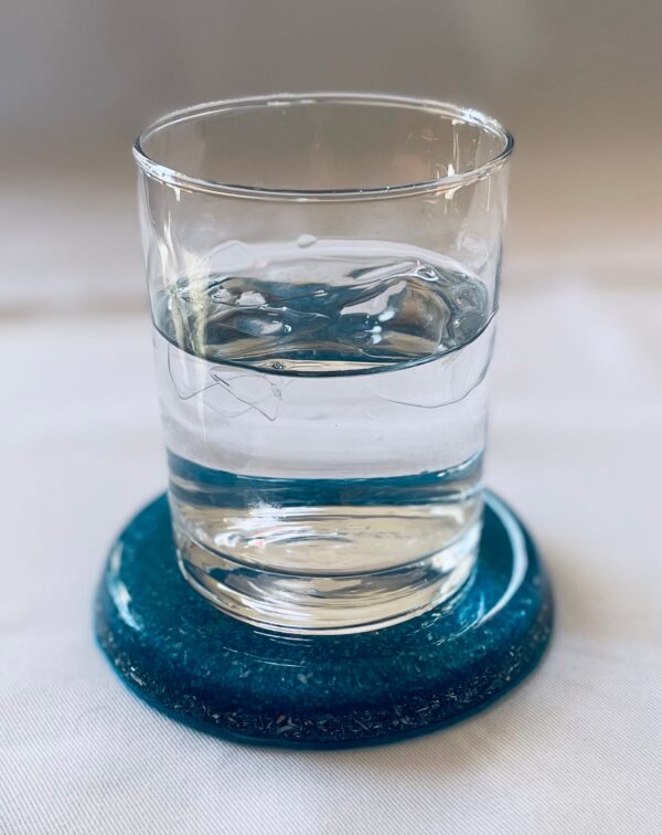 Clear glass with water sits on dark blue circular dolomite coaster on white surface