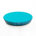 Dessous-de-verre orgonite turquoise rond avec surface lisse et bord cristallin texturé, photographié en angle sur fond blanc