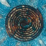 Dark spiral coil with metallic copper-colored edges on crushed blue crystal background with clear crystal points
