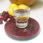Red speckled round orgonite plate with glass of lemon water, yellow lemons, and red cherries on white surface
