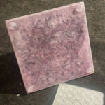 Baldosa cuadrada orgonite rosa-púrpura con 4 protuberancias en esquinas, textura cristalina jaspeada, junto a molde silicona blanco