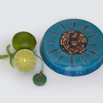 Blue circular orgonite disc with copper spiral center and radiating lines, beside lime halves and green tree pendant on white