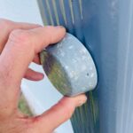 Hands holding blue-grey orgonite dome with embedded crystals and metallic flakes against blue cactus background
