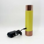 Yellow cylindrical device with copper-colored metal ends and black power adapter with cord on white background