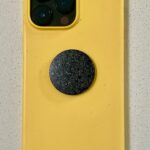 Yellow phone case with triple camera cutout, black circular disc with sparkly texture attached to back center