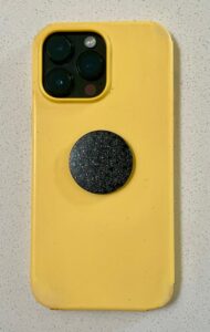 Yellow phone case with triple camera cutout, black circular disc with sparkly texture attached to back center