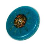Blue circular orgonite disc with golden spiral coil pattern in center, viewed from above on white background