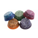 Cinco piezas de orgonite con forma de cúpula en azul, verde, rosa, naranja y morado con virutas metálicas sobre fondo blanco
