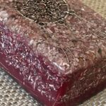 Dark red-purple orgonite brick with embedded metal coils and shavings, sitting on woven mat surface