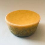 Disco orgonite redondo amarillo dorado con patrón grabado decorativo en el borde inferior, visto en ángulo sobre superficie blanca