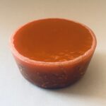 Cuenco orgonite redondo naranja-marrón con interior brillante y exterior texturizado, fotografiado desde arriba sobre fondo claro