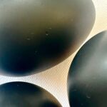 Three dark grey-black oval shungite eggs arranged on light wooden surface with visible grain pattern