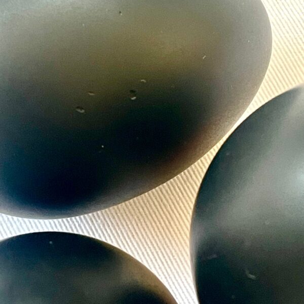Three dark grey-black oval shungite eggs arranged on light wooden surface with visible grain pattern