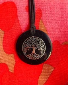 Black circular shungite pendant with silver tree of life design, on black cord against red and gold fabric background