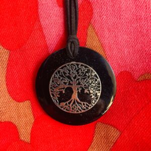 Black circular shungite pendant with silver tree of life design, on black cord against red and gold fabric background