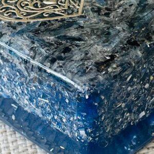 Dark blue-black orgonite brick with crystalline surface texture, viewed from above at an angle, with decorative metal trim visible