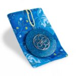 Pendentif orgonite circulaire bleu avec motif géométrique argenté, sur tissu bleu à motifs floraux, cordon jaune