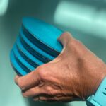 Hand holding stack of blue circular discs with dark layers between them, pool water visible in blurred background