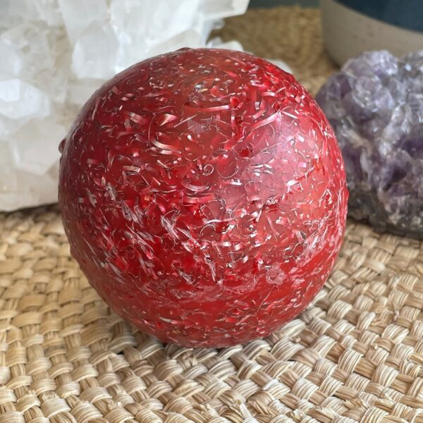Red translucent sphere with cracked glass-like texture on woven basket surface, white and purple crystals in background
