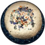 Spherical orgonite with cream-colored resin interior containing multicolored crystal chips, surrounded by dark blue translucent rim