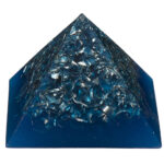 Pirámide orgonite azul con virutas metálicas y cristales incrustados por toda la superficie, vista en ángulo sobre fondo blanco
