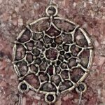 Golden metal dreamcatcher pendant with circular frame and intricate web pattern, photographed on purple crushed crystal background