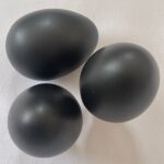 Three black oval shungite stones with smooth, polished surfaces arranged on white textured fabric background