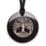 Black circular pendant with sparkly surface featuring tree of life design, hanging from black cord on white background