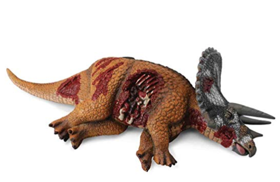 Toy dinosaur figure with brown and red coloring, appearing wounded or damaged, lying on its side against white background