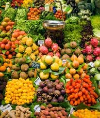 Colorful display of fresh fruits and vegetables at a market stall, including tomatoes, bananas, apples, and leafy greens