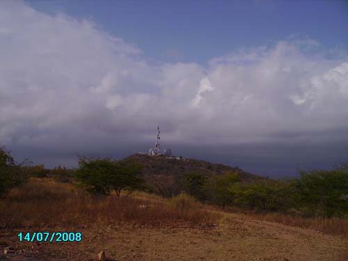 Dry landscape with sparse trees and a hill topped by a radio/cell tower under cloudy sky, dated 14/07/2008
